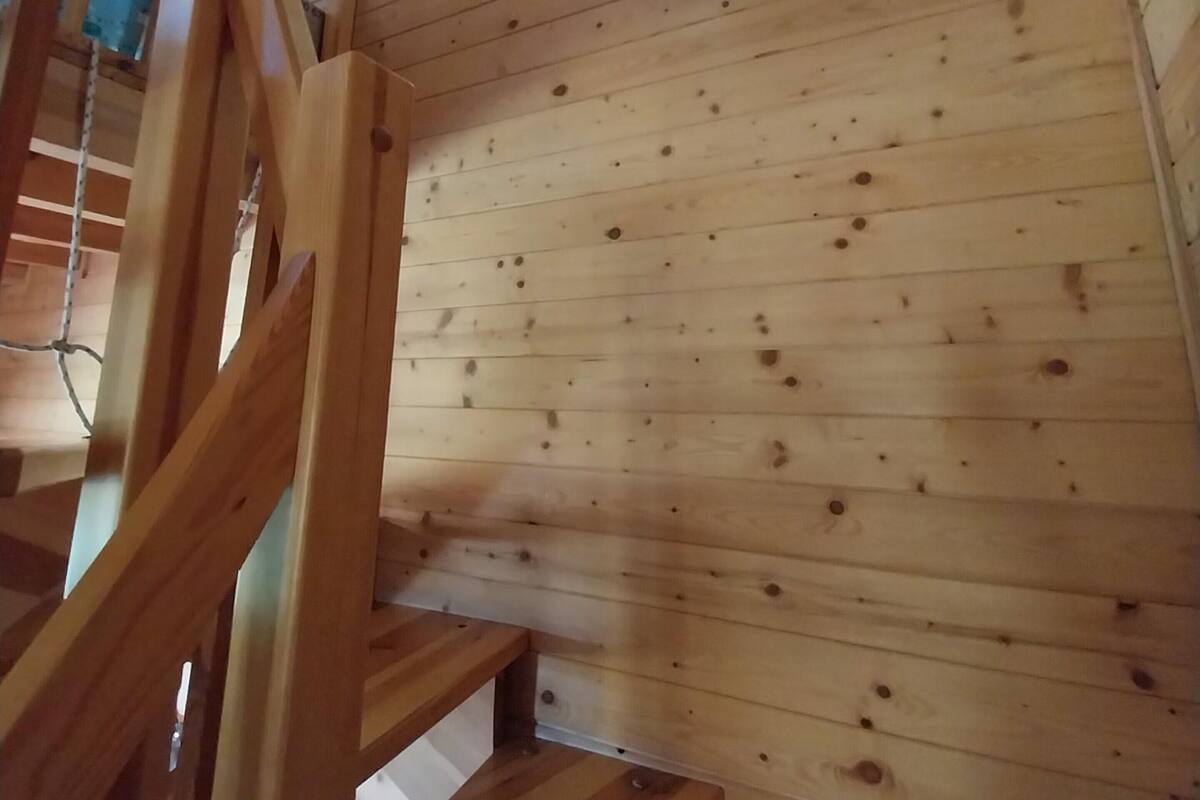 Eine Holztreppe mit Handlauf, die zu einem Raum mit schrägem Dach und einer runden Leuchte führt.