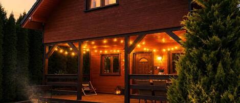 Una baita di legno con una veranda coperta, luci a stringa e un'area barbecue.