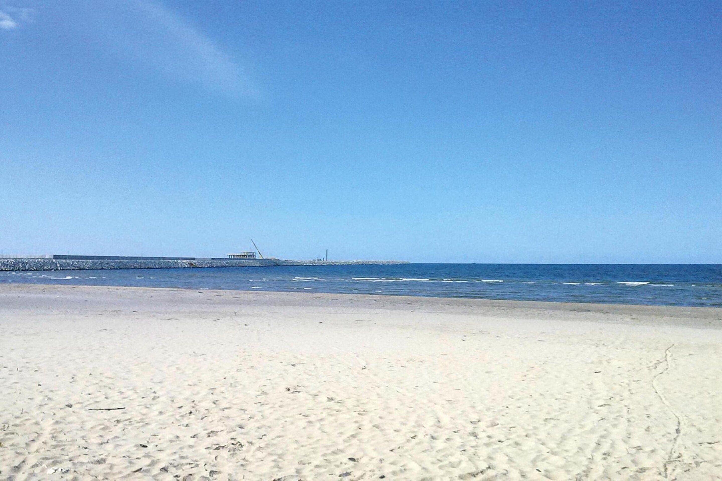 A beach with a clear sky and a rocky outcrop in the distance.