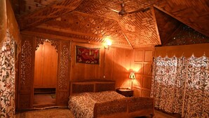 A wooden room with a bed, a nightstand, and a wall-mounted lamp. - Kings Houseboats (Srinagar)