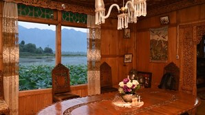 A wooden dining room with a large table, ornate chairs, and a view of a lake with mountains in the background. - Kings Houseboats (Srinagar)