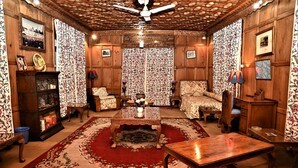 A traditional room with wooden paneling, a central coffee table, a sofa, and patterned curtains. - Kings Houseboats (Srinagar)