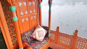 A traditional wooden balcony with intricate carvings, a cushioned seating area, and a small table with a decorative item. - Kings Houseboats (Srinagar)