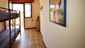 Une chambre avec des lits superposés, une fenêtre avec des rideaux, un tableau au mur et un sol carrelé.