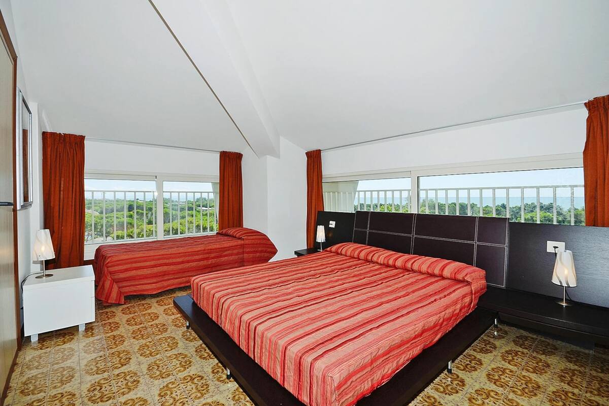 A hotel room with two beds, a large window with a view, a bedside table with a lamp, and a nightstand.