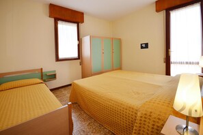 Une chambre d’hôtel avec un lit double, un lit simple, une armoire, une fenêtre avec des rideaux et une lampe de chevet.