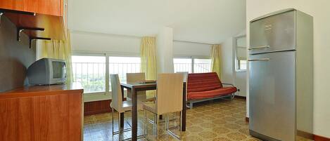 A compact room with a dining table, chairs, a sofa, a television, and a refrigerator.