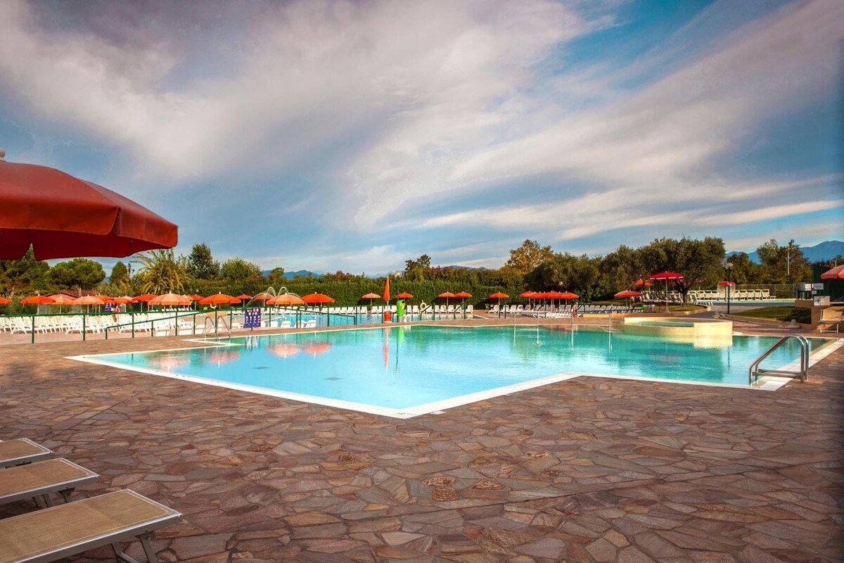 Une piscine entourée d’une terrasse en pierre, avec des chaises longues et des parasols.