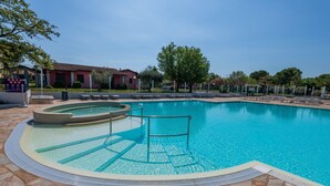Une piscine bordée de pierres, des chaises longues et un ciel d’un bleu limpide.