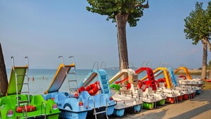 Une rangée de pédalos aux couleurs vives était alignée sur une plage de sable, avec des arbres et un ciel dégagé en arrière-plan.