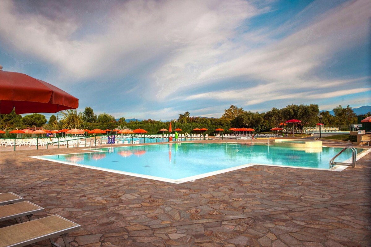 Une piscine entourée d’une terrasse dallée de pierres, avec des chaises longues et des parasols.