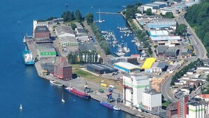 An aerial view of a coastal town with a marina, industrial buildings, and a large ship docked at the harbor. - Houseboat Leni, Flensburg (Flensburg)