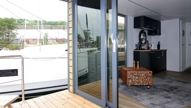 A modern interior with a sliding glass door leading to a balcony, a kitchen area with a microwave, and a small wooden table. - Houseboat Leni, Flensburg (Flensburg)