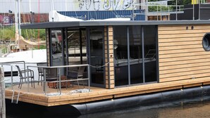A modern boat with a wooden deck, glass windows, and a covered seating area. - Houseboat Leni, Flensburg (Flensburg)