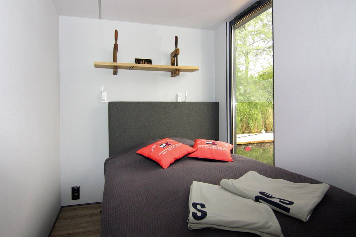 Une chambre moderne avec un grand lit, deux oreillers rouges et une vue sur la verdure.