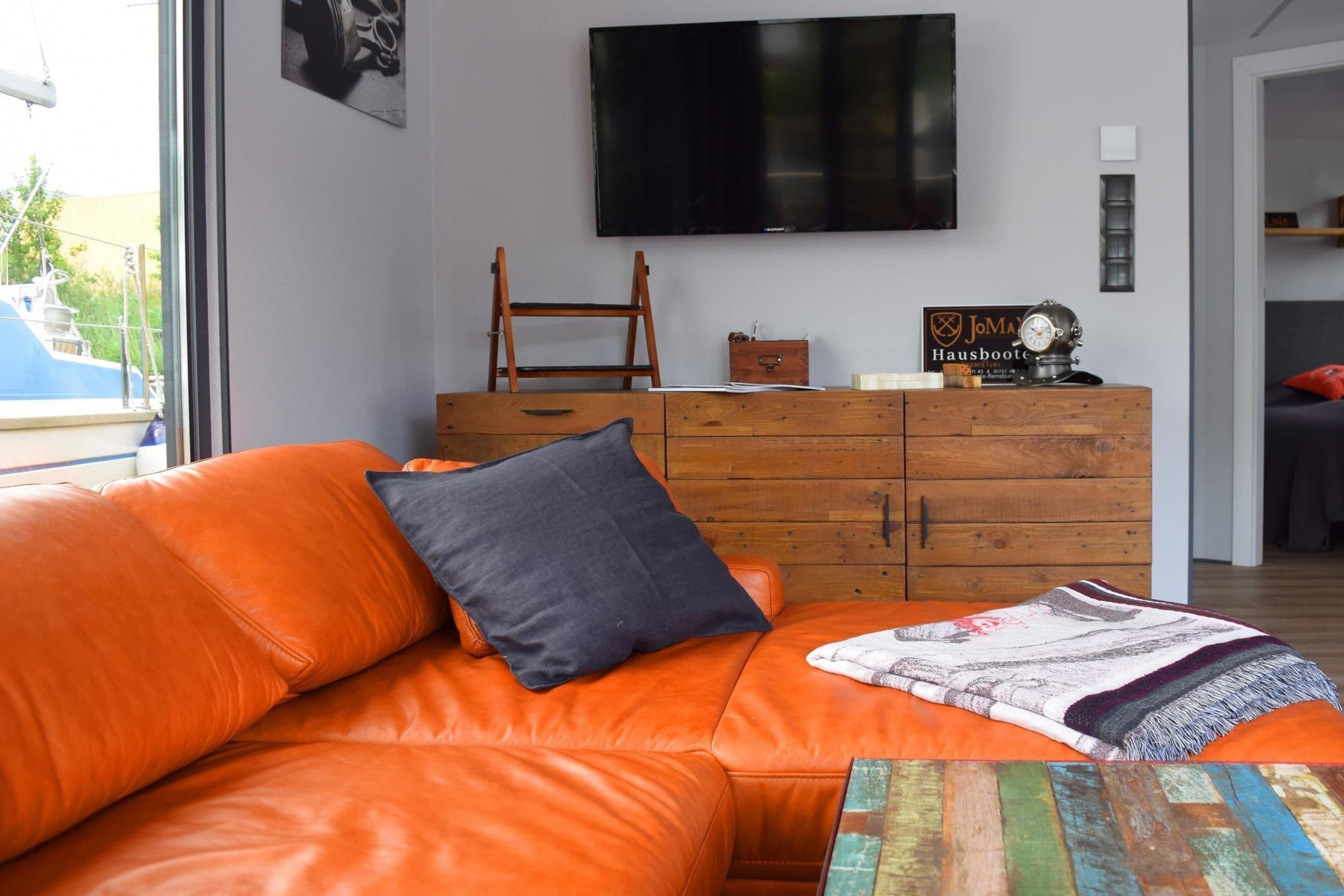 A living room with an orange leather sofa, a wooden dresser, and a flat-screen TV mounted on the wall.