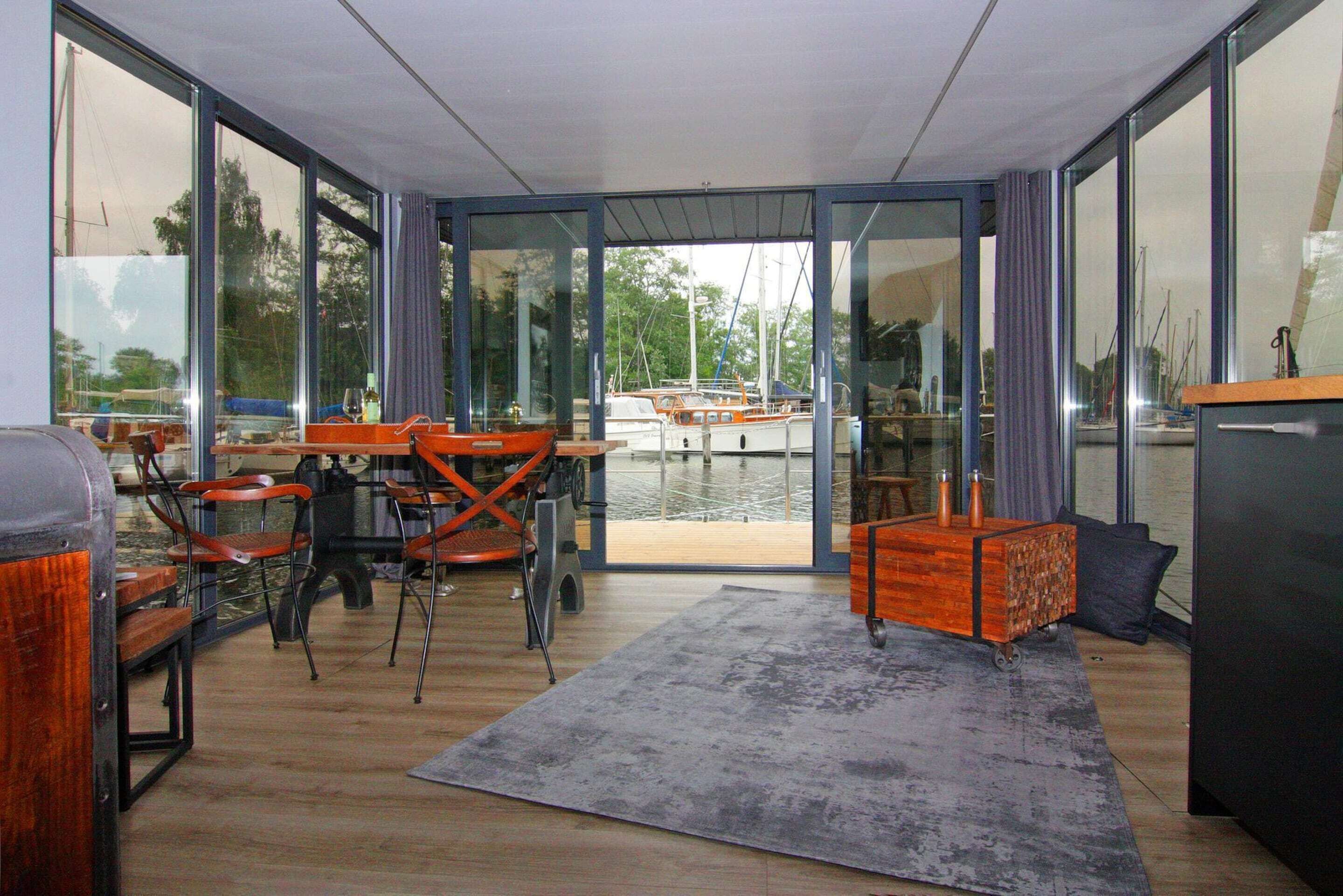 A modern interior with a dining area, a wooden cabinet, and a view of boats through large glass doors.