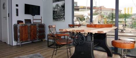 Un comedor con una mesa y sillas de madera, un taburete de estilo vintage y un ventanal con vistas a edificios y banderas.