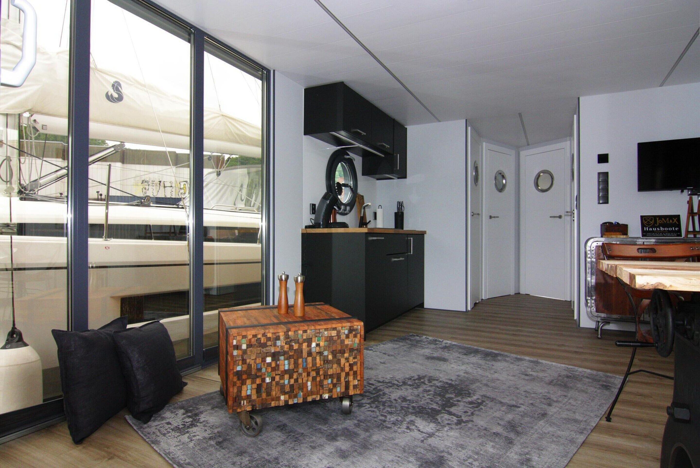 A modern kitchen with a large window, a wooden coffee table, and a grey rug.