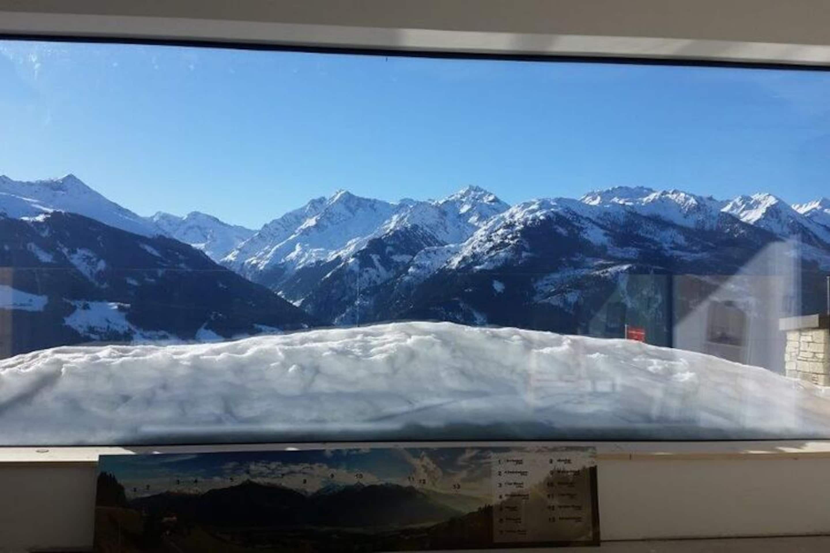 En vy över snötäckta berg genom ett fönster, med en klar himmel.