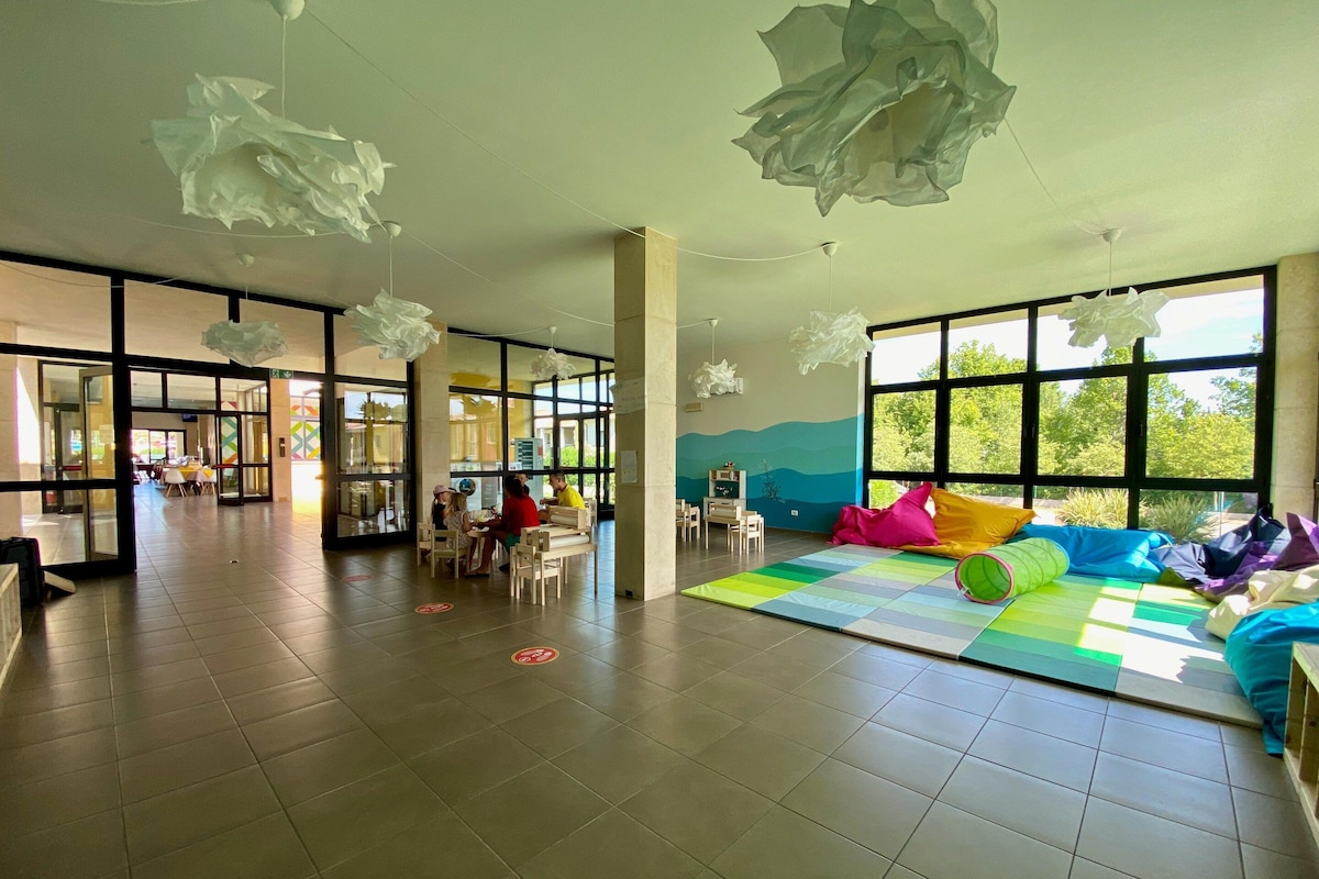 A spacious indoor area with large windows, a colorful play mat, and a seating area with cushions.
