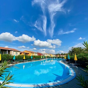 A swimming pool with lounge chairs and umbrellas, surrounded by buildings with red roofs.