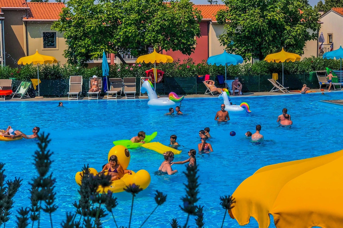 Piscina com brinquedos infláveis, cadeiras de descanso e guarda-sóis.