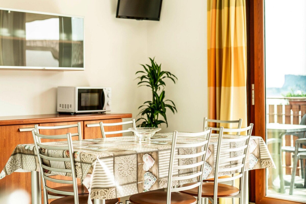 A dining area with a table set for four, surrounded by chairs, a potted plant, and a television mounted on the wall.