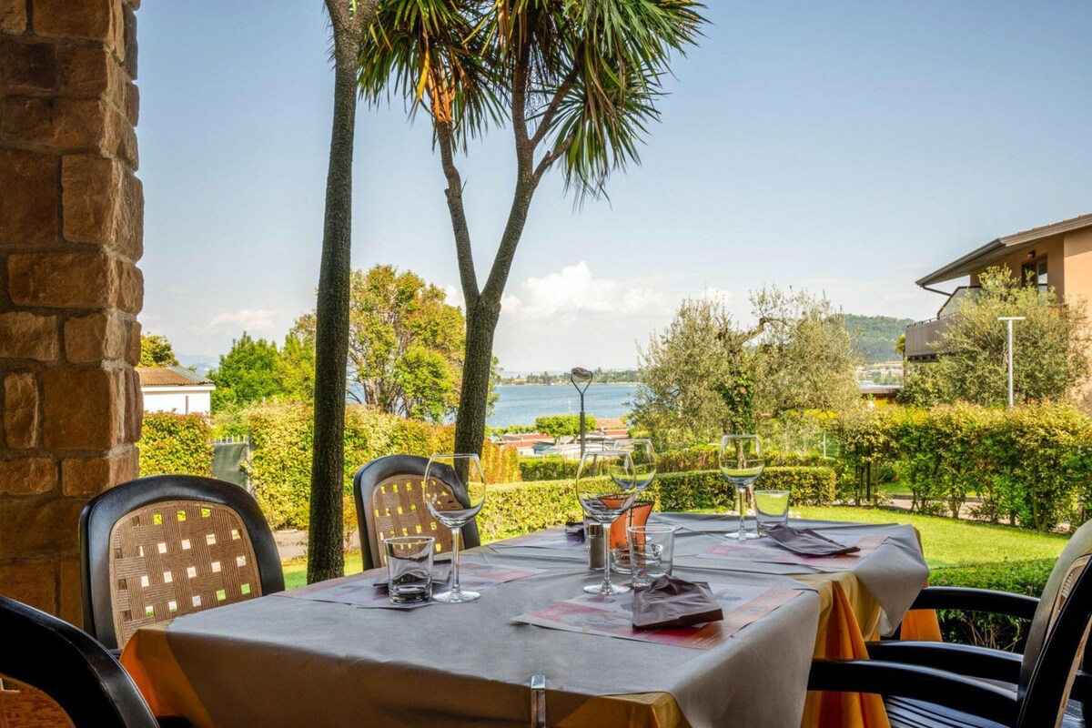 An outdoor dining area with tables set for two, overlooking a body of water and hills.