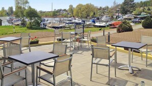 An outdoor patio with tables and chairs, overlooking a marina with boats. - Apartments at Heidensee, Schwerin (Schwerin)