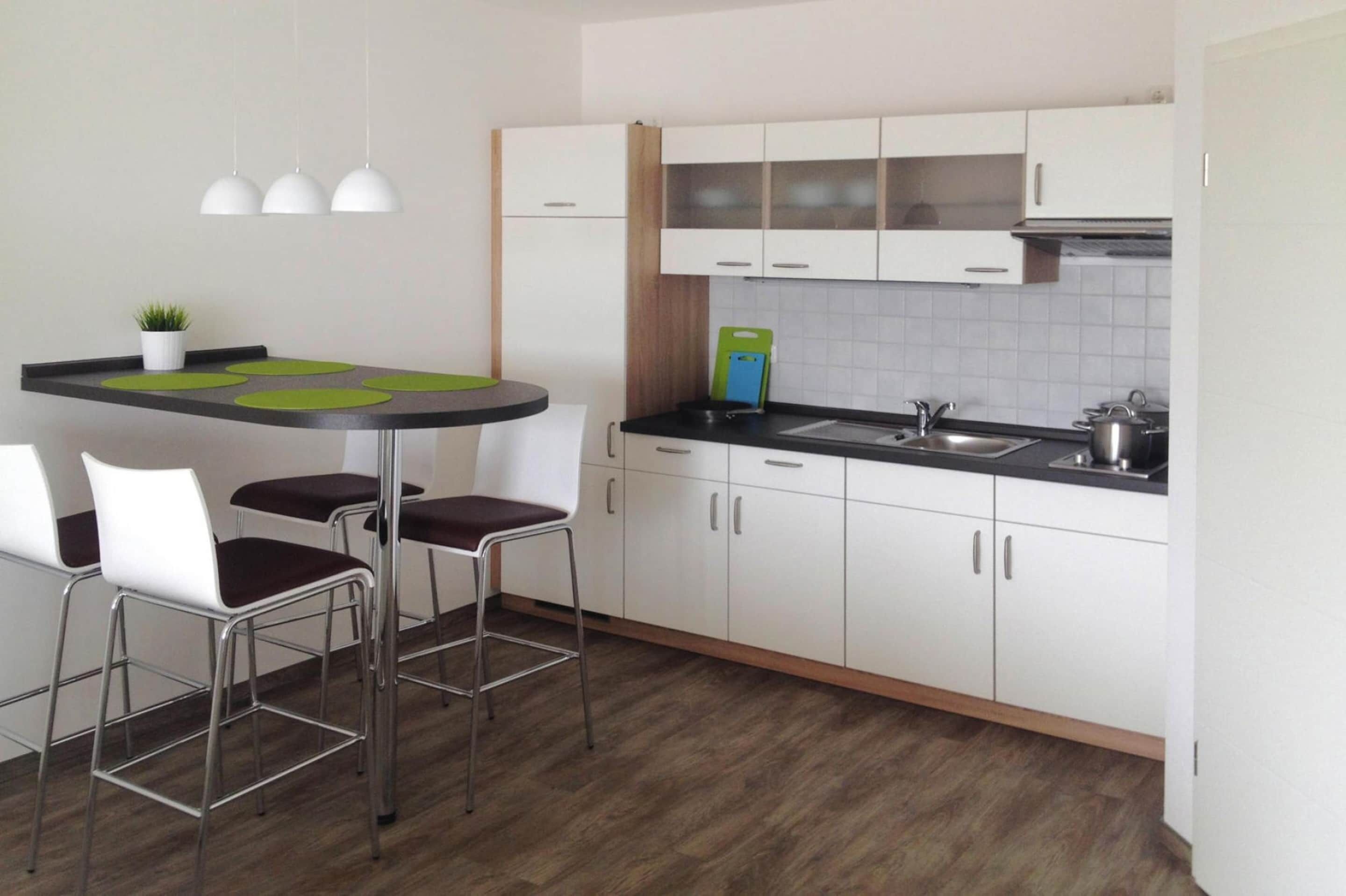 A modern kitchen with white cabinets, a black countertop, and a round table with bar stools.