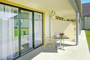 A modern outdoor patio with a glass door leading to a garden, a table with chairs, and a potted plant. - Apartments at Heidensee, Schwerin (Schwerin)