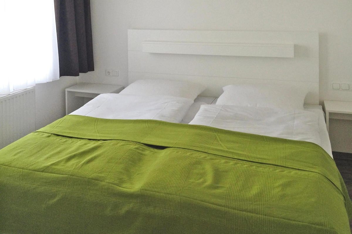 A hotel room with a bed, white headboard, and a green bedspread.