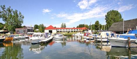 A marina with several boats docked, a building with a red roof, and trees in the background.