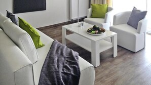 A modern living room with a white sofa, a coffee table with a plate of food, and a white armchair. - Apartments at Heidensee, Schwerin (Schwerin)