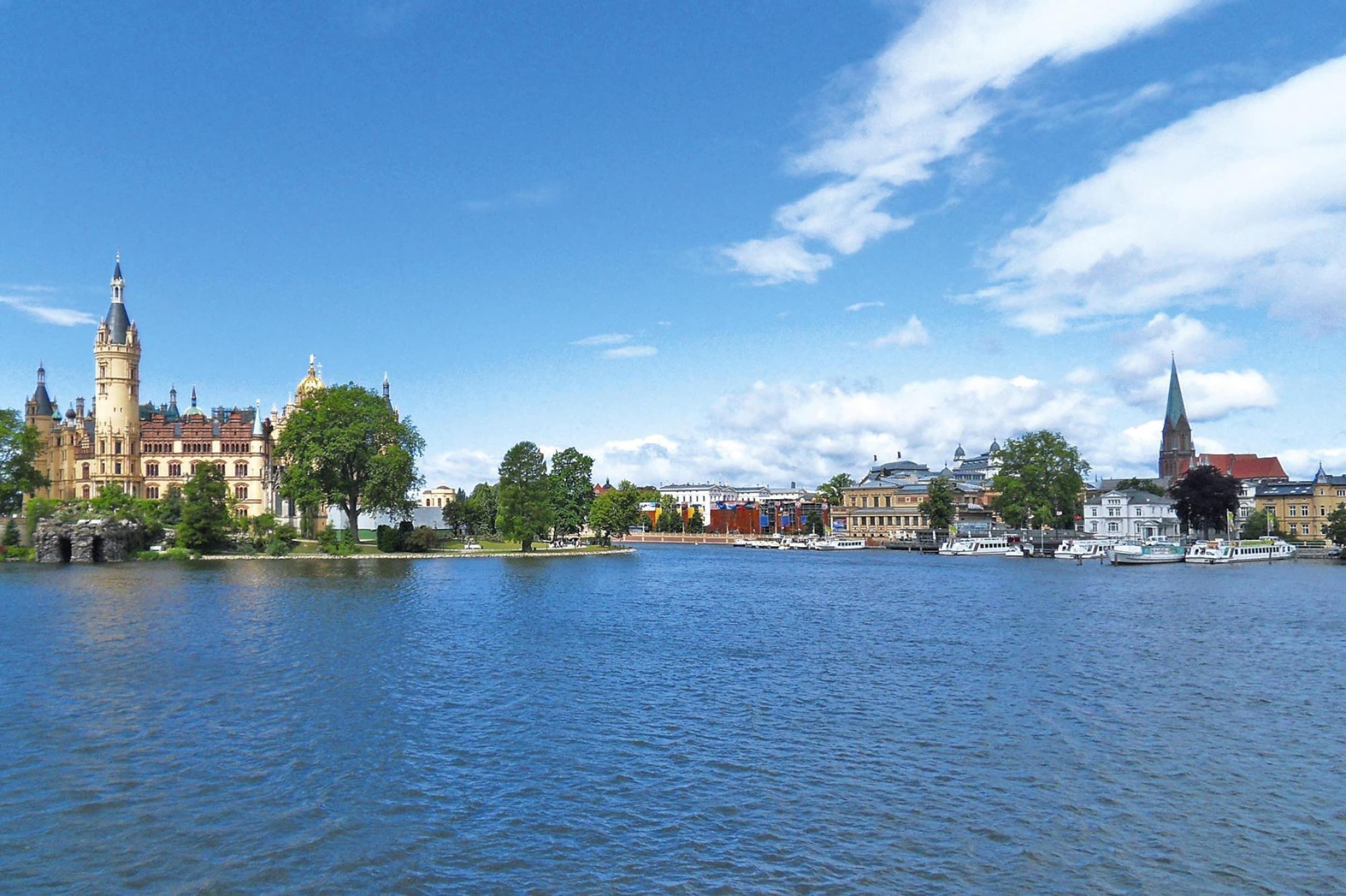 A riverside view of historic buildings, including a prominent tower and a church, with boats docked along the water.