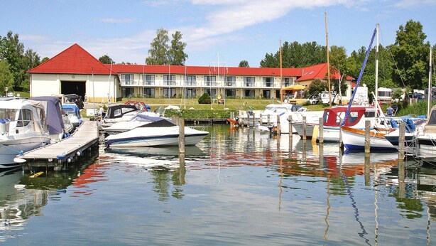 A marina with boats docked, a building with a red roof, and a clear sky. - Apartments at Heidensee, Schwerin (Schwerin)