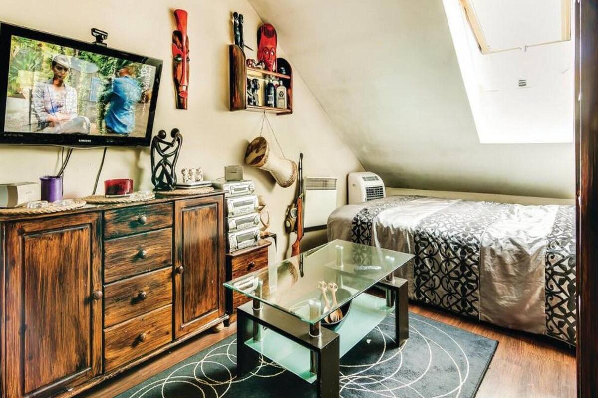 Una habitación pequeña y acogedora con una cama en altillo, una mesita de centro de vidrio, un aparador de madera y un televisor montado en la pared.