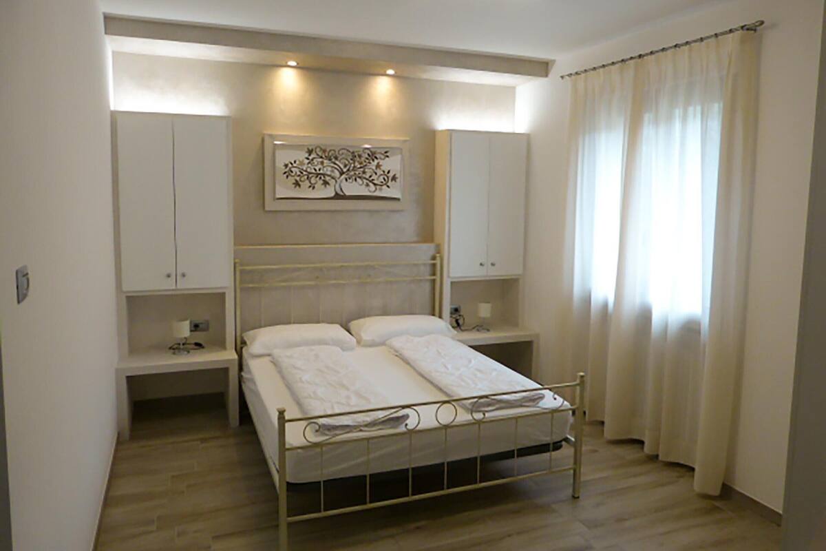 A bedroom with a bed, bedside tables, a nightstand, a wall-mounted artwork, and a window with curtains.