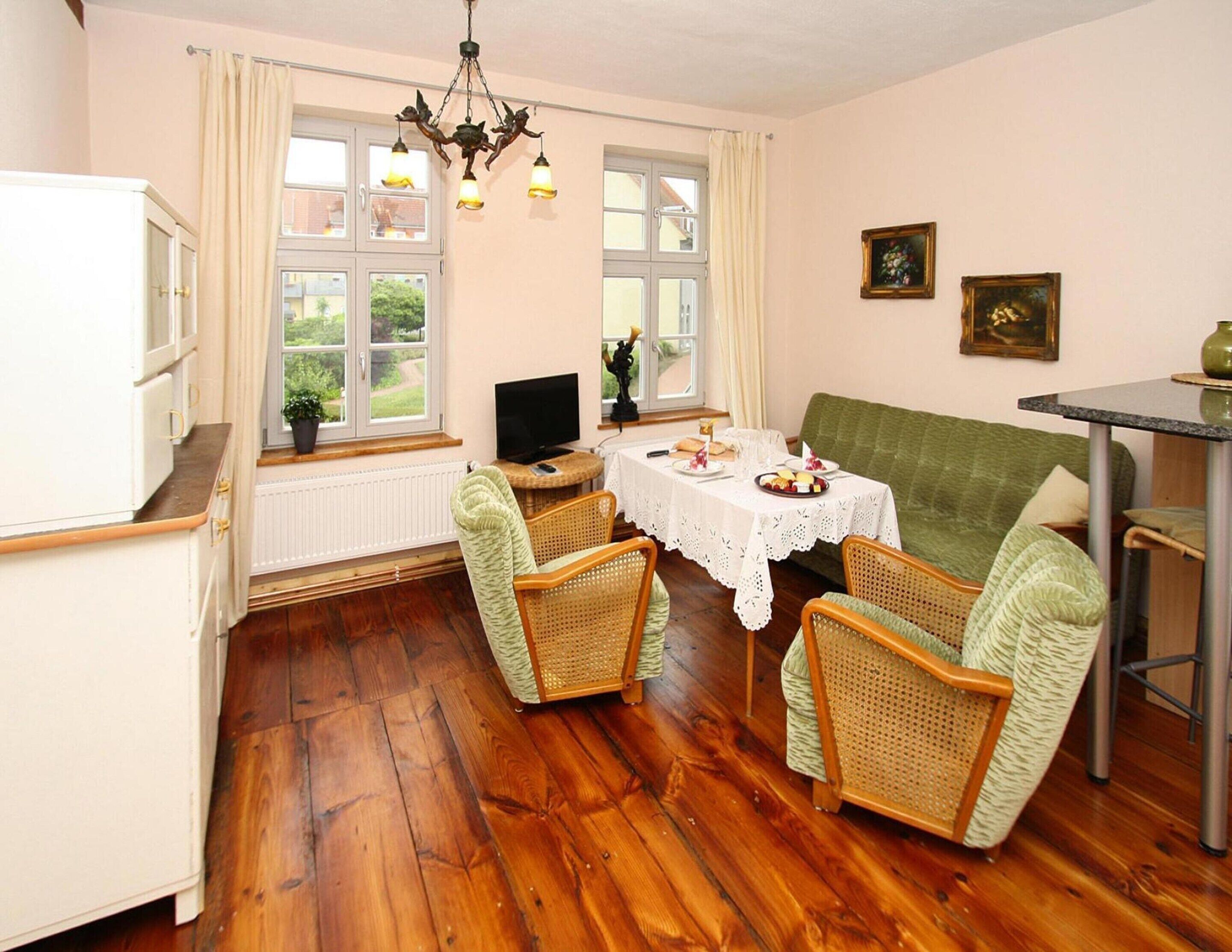 A cozy dining area with a table set for two, surrounded by wicker chairs, a green sofa, and a television on a small table.