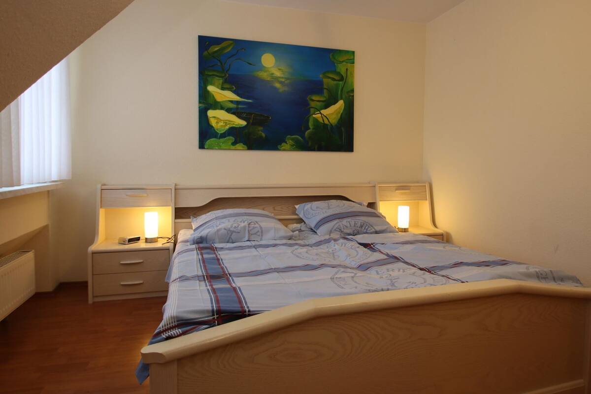 Une chambre à coucher avec un lit, deux tables de chevet, une commode et un tableau accroché au mur.