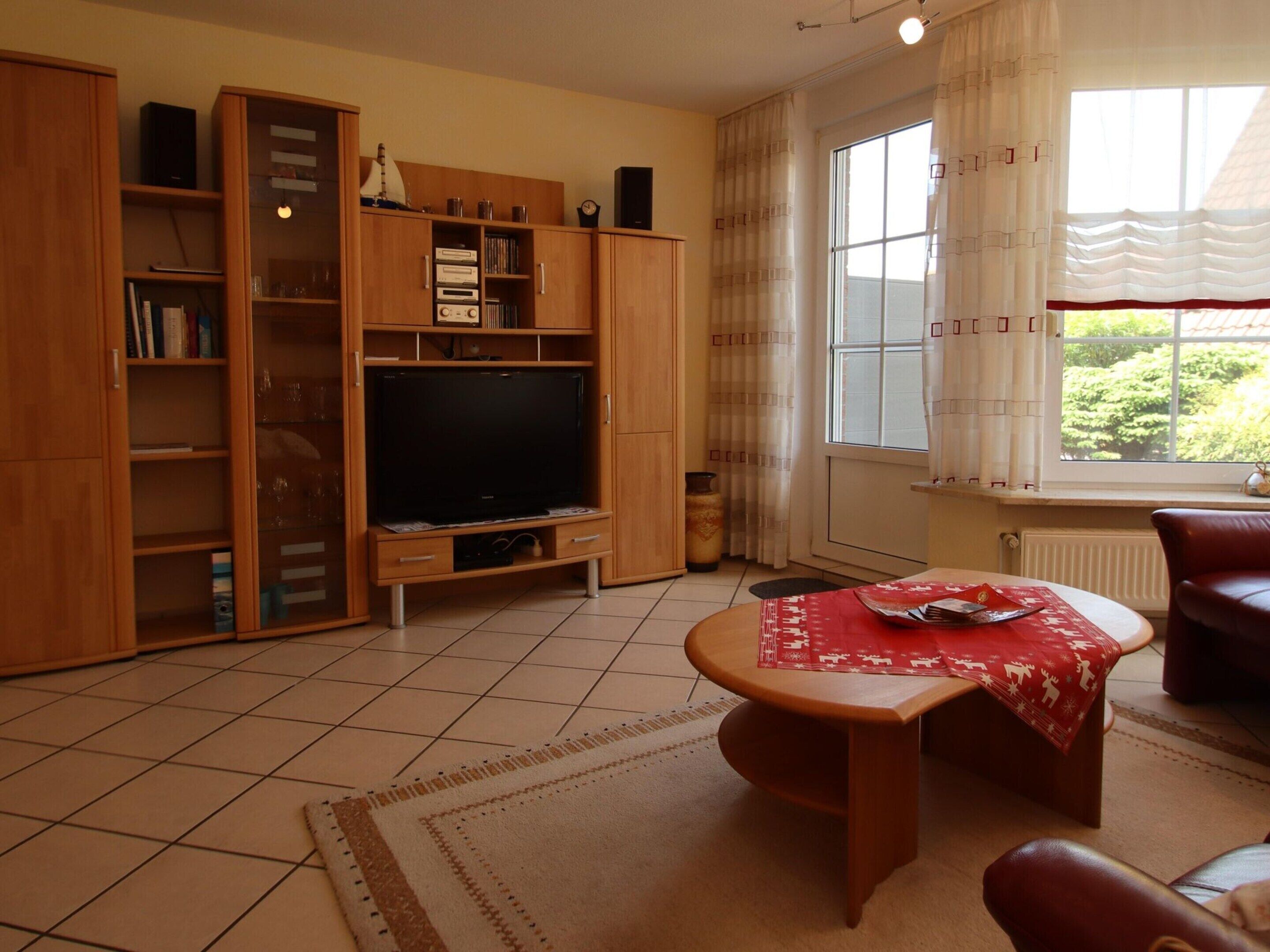 Ein Wohnzimmer mit Fernseher, Holzschränken, einem roten Tisch und einem Fenster mit Vorhängen.