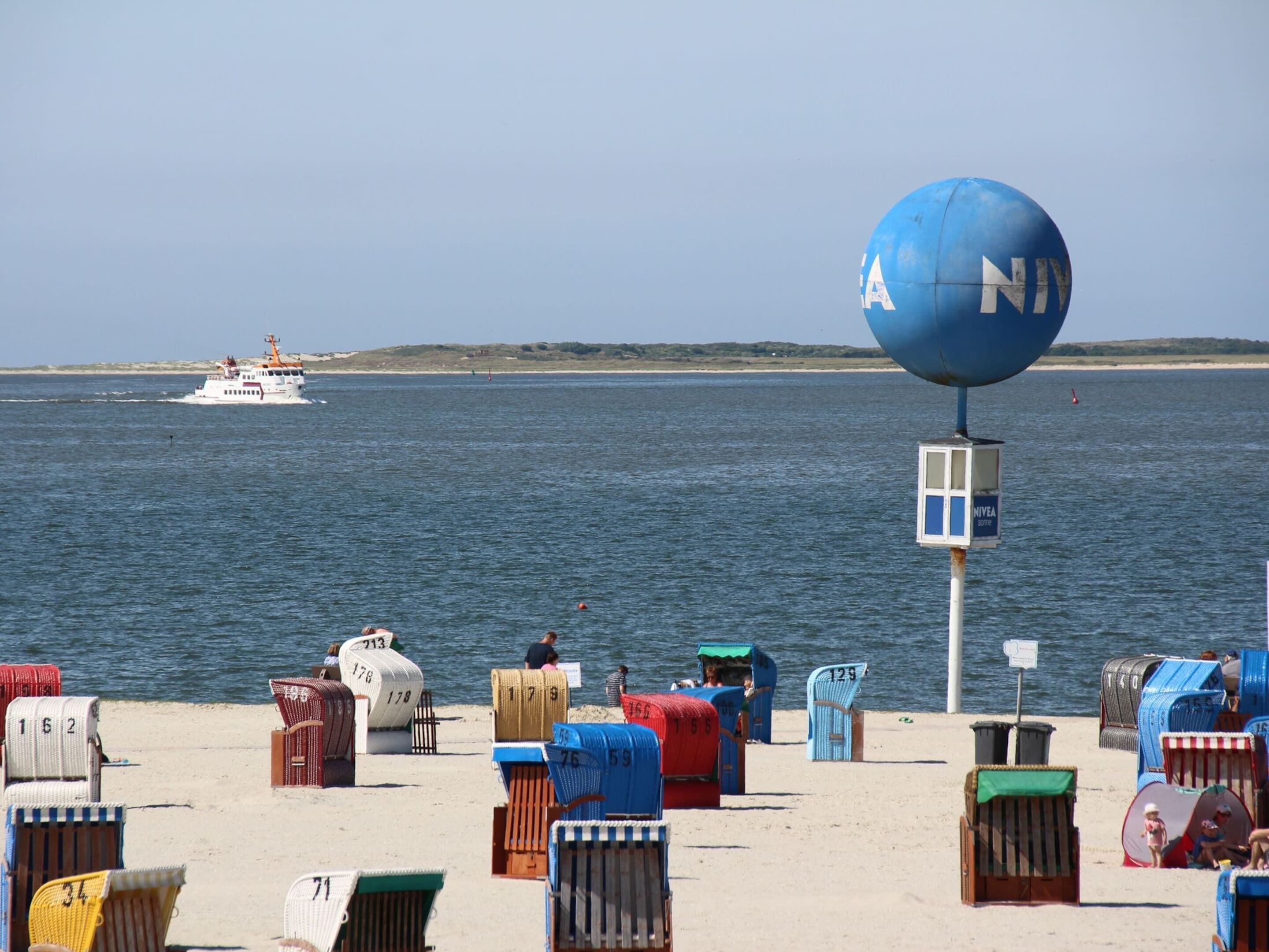 A beach with numbered beach chairs and a large blue ball structure.