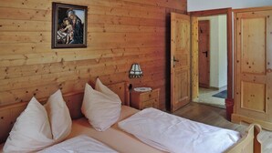 A wooden room with a bed, pillows, a nightstand, a lamp, and a door. - Apartment in Fusch an der Glocknerstrasse in Nature (Fusch an der Grossglocknerstrasse)