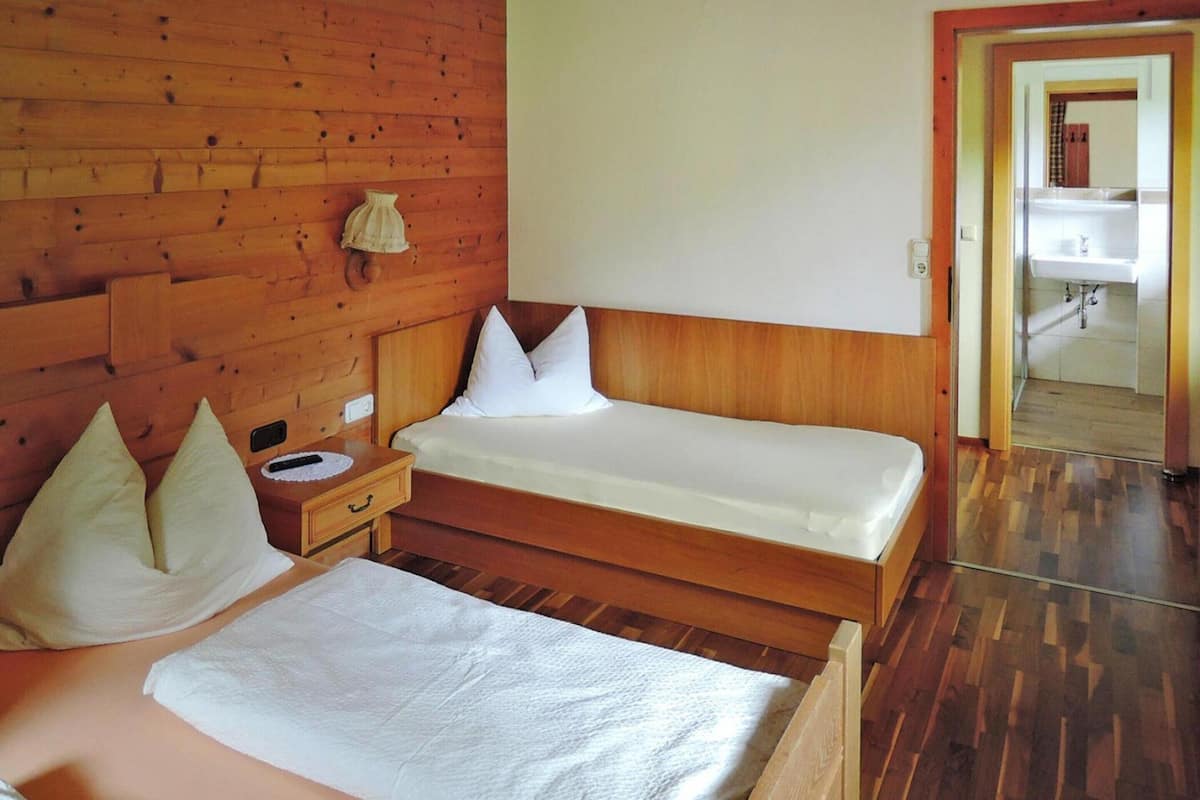 A wooden room with a bed, a nightstand, and a bathroom visible through an open door.