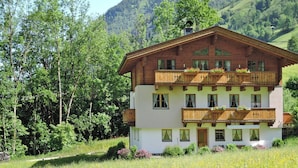 A two-story wooden chalet with balconies, surrounded by lush greenery and mountains. - Apartment in Fusch an der Glocknerstrasse in Nature (Fusch an der Grossglocknerstrasse)