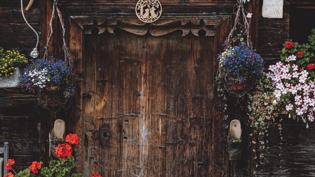 A rustic wooden door with a decorative plate above it, flanked by potted plants with flowers. - Apartment in Fusch an der Glocknerstrasse in Nature (Fusch an der Grossglocknerstrasse)