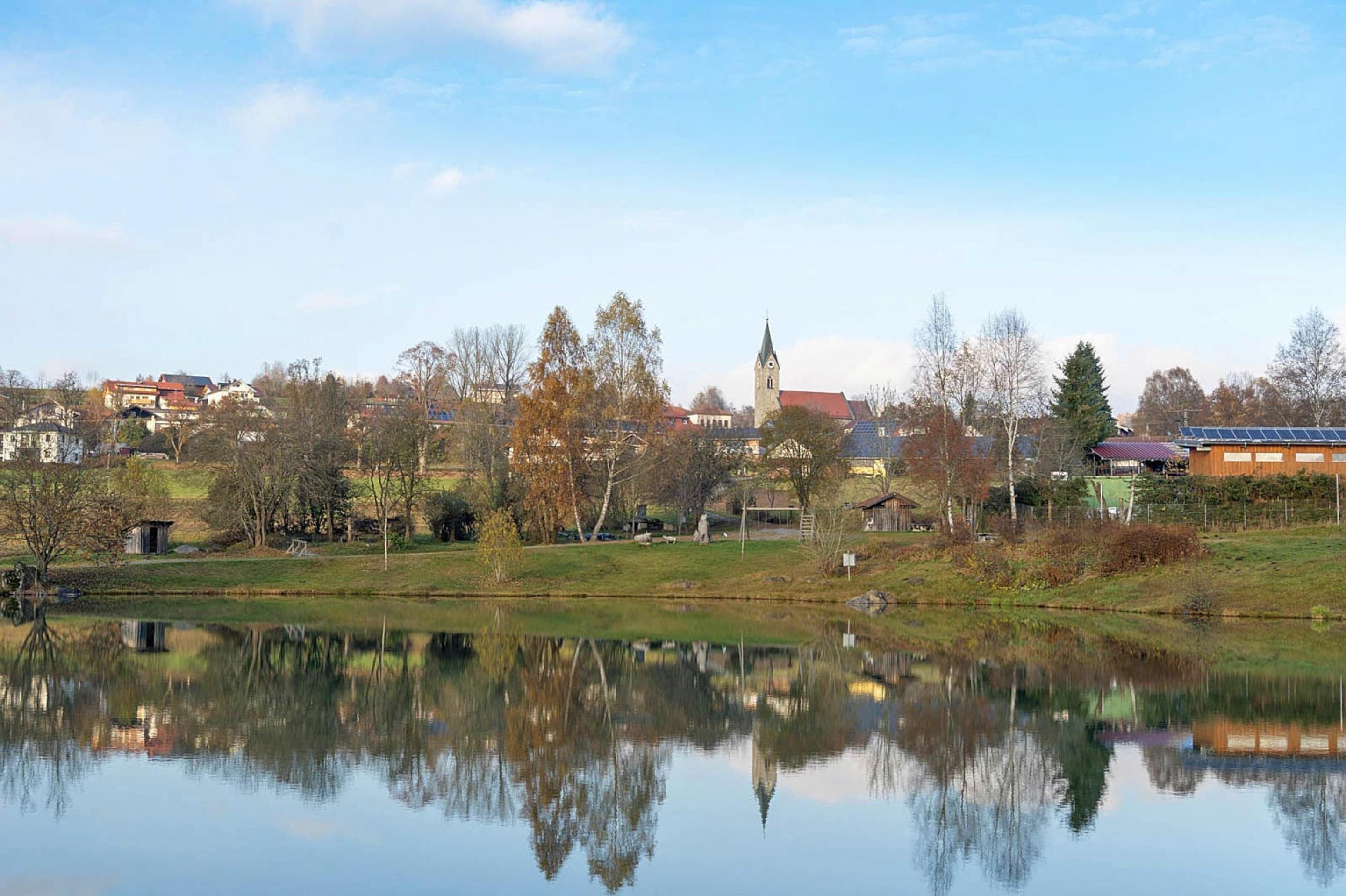 A serene lakeside view with a church, residential buildings, and a small dock.