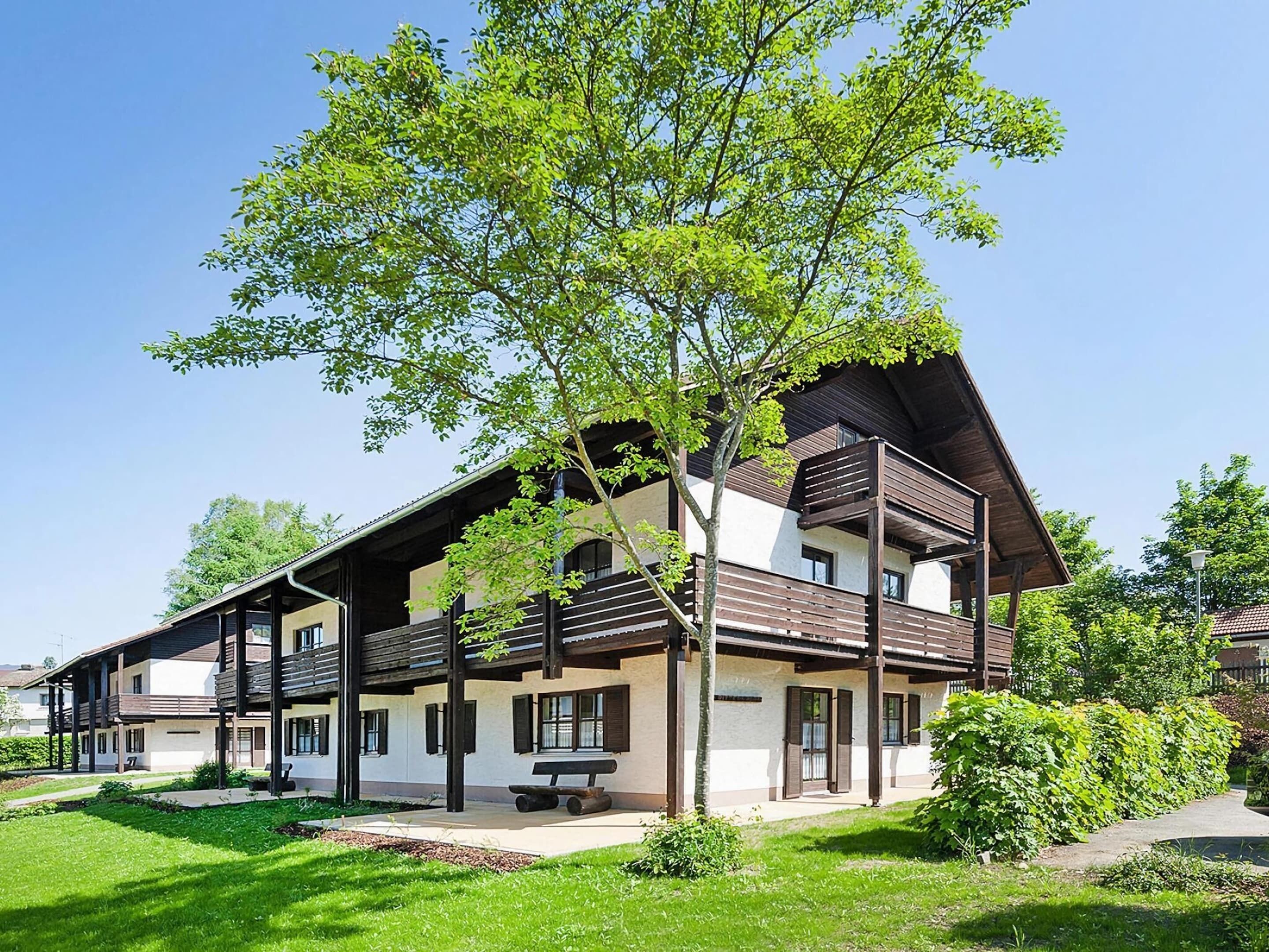 A two-story building with a balcony, a bench, and a tree in front.