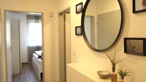 A hallway with a wooden floor, a round mirror on the wall, and a small plant on a console table. - Apartment in a Quiet Location in Dornumersiel (Dornum)